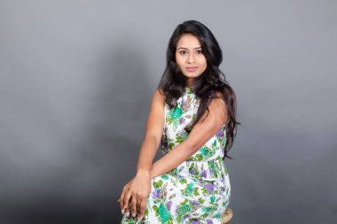 Kendine güvenen, çiçekli bluz giyen genç bir kadın zarif bir şekilde stüdyo ortamında poz veriyor. Güzelliğini, kendine güvenini ve tarzını sergiliyor. Onun uzun saçları zarif bir şekilde akıyor, resme hareketlilik ve canlılık katıyor.