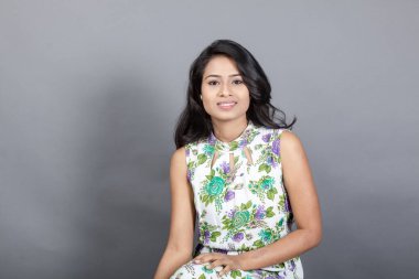 Kendine güvenen, çiçekli bluz giyen genç bir kadın zarif bir şekilde stüdyo ortamında poz veriyor. Güzelliğini, kendine güvenini ve tarzını sergiliyor. Onun uzun saçları zarif bir şekilde akıyor, resme hareketlilik ve canlılık katıyor.