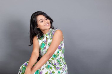 Kendine güvenen, çiçekli bluz giyen genç bir kadın zarif bir şekilde stüdyo ortamında poz veriyor. Güzelliğini, kendine güvenini ve tarzını sergiliyor. Onun uzun saçları zarif bir şekilde akıyor, resme hareketlilik ve canlılık katıyor.