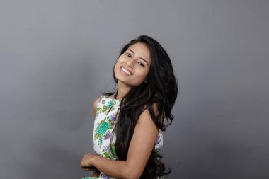 Kendine güvenen, çiçekli bluz giyen genç bir kadın zarif bir şekilde stüdyo ortamında poz veriyor. Güzelliğini, kendine güvenini ve tarzını sergiliyor. Onun uzun saçları zarif bir şekilde akıyor, resme hareketlilik ve canlılık katıyor.