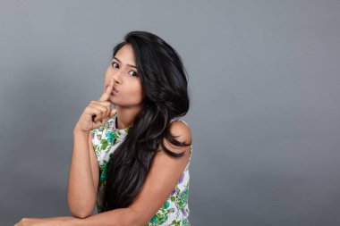 Kendine güvenen, çiçekli bluz giyen genç bir kadın zarif bir şekilde stüdyo ortamında poz veriyor. Güzelliğini, kendine güvenini ve tarzını sergiliyor. Onun uzun saçları zarif bir şekilde akıyor, resme hareketlilik ve canlılık katıyor.