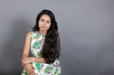 Kendine güvenen, çiçekli bluz giyen genç bir kadın zarif bir şekilde stüdyo ortamında poz veriyor. Güzelliğini, kendine güvenini ve tarzını sergiliyor. Onun uzun saçları zarif bir şekilde akıyor, resme hareketlilik ve canlılık katıyor.