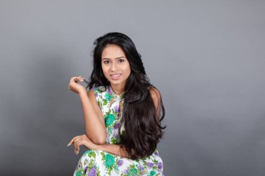 Kendine güvenen, çiçekli bluz giyen genç bir kadın zarif bir şekilde stüdyo ortamında poz veriyor. Güzelliğini, kendine güvenini ve tarzını sergiliyor. Onun uzun saçları zarif bir şekilde akıyor, resme hareketlilik ve canlılık katıyor.