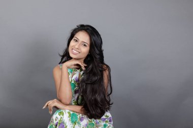 Kendine güvenen, çiçekli bluz giyen genç bir kadın zarif bir şekilde stüdyo ortamında poz veriyor. Güzelliğini, kendine güvenini ve tarzını sergiliyor. Onun uzun saçları zarif bir şekilde akıyor, resme hareketlilik ve canlılık katıyor.