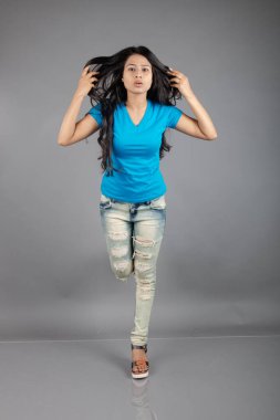 Genç bir kadın özgüvenle mavi tişört, sıkıntılı kot pantolon, topuklu ayakkabı giyerek poz veriyor, cazibe ve zarafetle gelişigüzel bir şehir tarzı sergiliyor, saç bakımı, özgürlük, kendini ifade etme projesi için uygun.,.