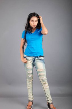 Genç bir kadın özgüvenle mavi tişört, sıkıntılı kot pantolon, topuklu ayakkabı giyerek poz veriyor, cazibe ve zarafetle gelişigüzel bir şehir tarzı sergiliyor, saç bakımı, özgürlük, kendini ifade etme projesi için uygun.,.