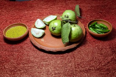 Canlı yeşil guava (bütün ve dilimlenmiş), yeşil biber ve Kasundi (popüler bir Bengali baharatlı hardal sosu) toprak kaselerinde sunulmaktadır.