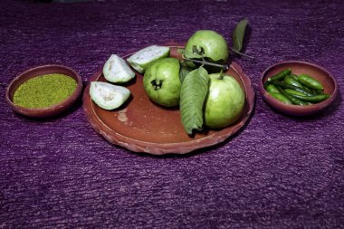 Canlı yeşil guava (bütün ve dilimlenmiş), yeşil biber ve Kasundi (popüler bir Bengali baharatlı hardal sosu) toprak kaselerinde sunulmaktadır.