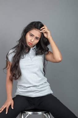 Gündelik iş kıyafetleri giymiş kendine güvenen bir kadın stüdyo ortamında modern bir taburede oturuyor, profesyonelliği, zarafeti ve moda veya iş temalı projeler için uygun duruşu çağrıştırıyor..