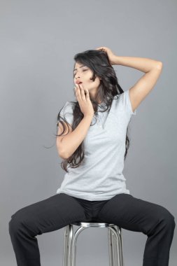 Gündelik iş kıyafetleri giymiş kendine güvenen bir kadın stüdyo ortamında modern bir taburede oturuyor, profesyonelliği, zarafeti ve moda veya iş temalı projeler için uygun duruşu çağrıştırıyor..