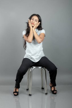 Gündelik iş kıyafetleri giymiş kendine güvenen bir kadın stüdyo ortamında modern bir taburede oturuyor, profesyonelliği, zarafeti ve moda veya iş temalı projeler için uygun duruşu çağrıştırıyor..