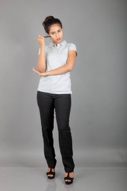 Neşeli bir ofis hanımı ya da kalemle poz veren genç bir üniversite öğrencisi. Yarı resmi giyinmiş genç bir kadın gri polo tişört giyiyor, siyah pantolon ve gri arka plan..