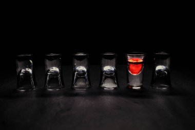 Barın tezgahındaki boş kadehlerin arasında kırmızı renkli likörle dolu shot bardağı.