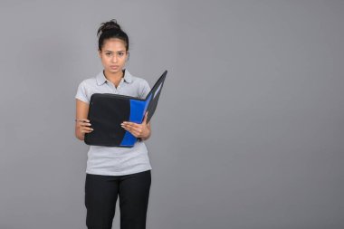 Neşeli ofis çalışanı ya da elinde bir dosya, kalem ve sunum tutan genç bir üniversite öğrencisi. Resmi giyinmiş genç bir kadın gri polo tişört giyiyor, siyah pantolon ve gri arka plan..
