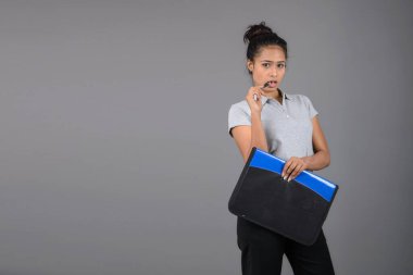 Neşeli ofis çalışanı ya da elinde bir dosya, kalem ve sunum tutan genç bir üniversite öğrencisi. Resmi giyinmiş genç bir kadın gri polo tişört giyiyor, siyah pantolon ve gri arka plan..