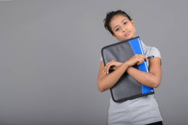 Neşeli ofis çalışanı ya da elinde bir dosya, kalem ve sunum tutan genç bir üniversite öğrencisi. Resmi giyinmiş genç bir kadın gri polo tişört giyiyor, siyah pantolon ve gri arka plan..