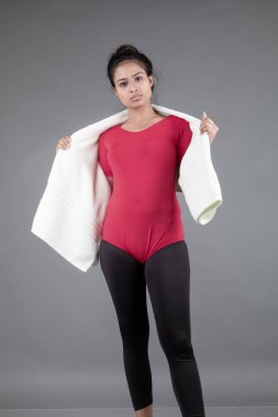 Kırmızı tişörtlü, siyah taytlı, aerobik egzersizi yapan, beyaz havluyla egzersiz yapan, gri arka planda izole edilmiş sağlıklı genç bir kadın.