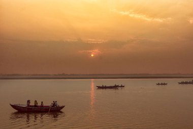 Huzurlu bir gün doğumu, gün batımı sıcak nehir manzarası ve teknelerde insanlar. Ganga nehir kıyısı. Varanasi, Hindistan.