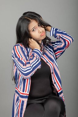 Üzgün Hintli genç kadın portresi somurtuyor, somurtuyor ve üzgün görünüyor, üzgün yüz ifadesi, gri arka plana karşı kasvetli duruyor.