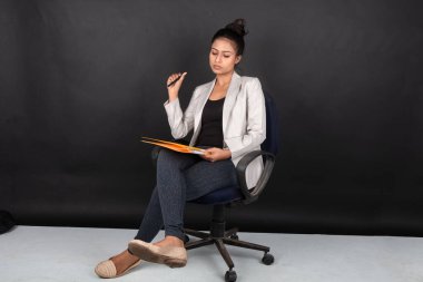 Yorgun ve endişeli genç bayan manken, beyaz ceket giyiyor, siyah bluz ve siyah kot pantolon giyiyor, elinde klasör olan bir sandalyede oturuyor. Reklam için ateş et..