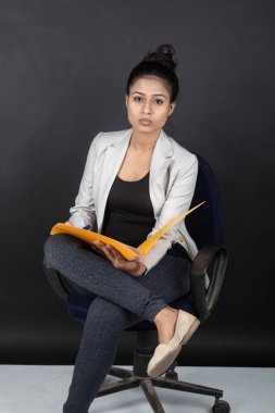 Yorgun ve endişeli genç bayan manken, beyaz ceket giyiyor, siyah bluz ve siyah kot pantolon giyiyor, elinde klasör olan bir sandalyede oturuyor. Reklam için ateş et..