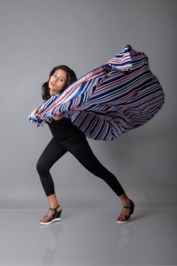 Siyah tayt giyen güzel, genç bir Hintli kadın, siyah üst ve kırmızı, mavi, beyaz çizgili tunik. Bir stüdyoda kutlama yapmak için gülüyor, dönüyor, zıplıyor ve dans ediyor.