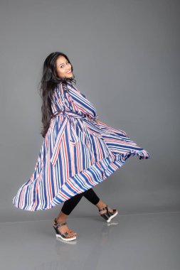 Siyah tayt giyen güzel, genç bir Hintli kadın, siyah üst ve kırmızı, mavi, beyaz çizgili tunik. Bir stüdyoda kutlama yapmak için gülüyor, dönüyor, zıplıyor ve dans ediyor.