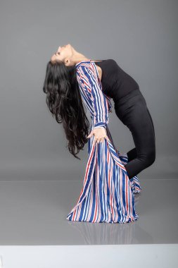 Siyah tayt giyen güzel, genç bir Hintli kadın, siyah üst ve kırmızı, mavi, beyaz çizgili tunik. Bir stüdyoda kutlama yapmak için gülüyor, dönüyor, zıplıyor ve dans ediyor.