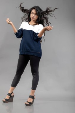 Gri arka planda günlük kışlık giysili Hintli genç bayan model. Siyah tayt giyen uzun siyah saçlı bir manken, mavi beyaz bir kazak..