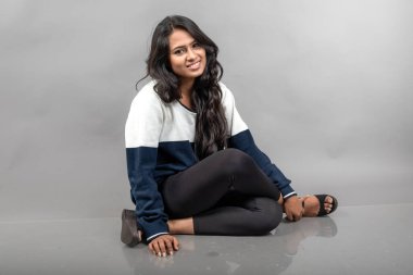 Gri arka planda günlük kışlık giysili Hintli genç bayan model. Siyah tayt giyen uzun siyah saçlı bir manken, mavi beyaz bir kazak..