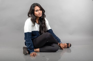 Gri arka planda günlük kışlık giysili Hintli genç bayan model. Siyah tayt giyen uzun siyah saçlı bir manken, mavi beyaz bir kazak..