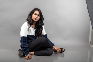 Gri arka planda günlük kışlık giysili Hintli genç bayan model. Siyah tayt giyen uzun siyah saçlı bir manken, mavi beyaz bir kazak..