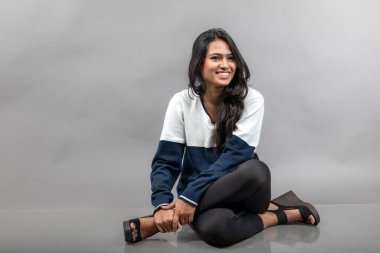 Gri arka planda günlük kışlık giysili Hintli genç bayan model. Siyah tayt giyen uzun siyah saçlı bir manken, mavi beyaz bir kazak..