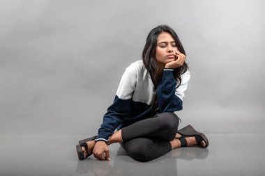 Gri arka planda günlük kışlık giysili Hintli genç bayan model. Siyah tayt giyen uzun siyah saçlı bir manken, mavi beyaz bir kazak..