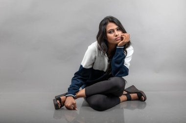 Gri arka planda günlük kışlık giysili Hintli genç bayan model. Siyah tayt giyen uzun siyah saçlı bir manken, mavi beyaz bir kazak..