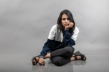 Gri arka planda günlük kışlık giysili Hintli genç bayan model. Siyah tayt giyen uzun siyah saçlı bir manken, mavi beyaz bir kazak..