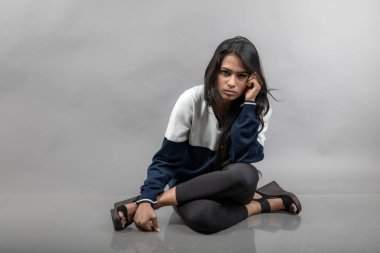 Gri arka planda günlük kışlık giysili Hintli genç bayan model. Siyah tayt giyen uzun siyah saçlı bir manken, mavi beyaz bir kazak..