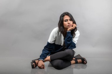 Gri arka planda günlük kışlık giysili Hintli genç bayan model. Siyah tayt giyen uzun siyah saçlı bir manken, mavi beyaz bir kazak..