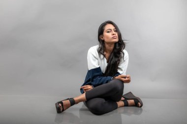 Gri arka planda günlük kışlık giysili Hintli genç bayan model. Siyah tayt giyen uzun siyah saçlı bir manken, mavi beyaz bir kazak..