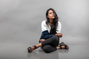 Gri arka planda günlük kışlık giysili Hintli genç bayan model. Siyah tayt giyen uzun siyah saçlı bir manken, mavi beyaz bir kazak..