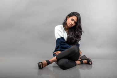 Gri arka planda günlük kışlık giysili Hintli genç bayan model. Siyah tayt giyen uzun siyah saçlı bir manken, mavi beyaz bir kazak..