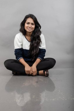 Gri arka planda günlük kışlık giysili Hintli genç bayan model. Siyah tayt giyen uzun siyah saçlı bir manken, mavi beyaz bir kazak..