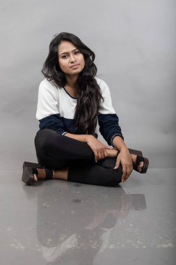 Gri arka planda günlük kışlık giysili Hintli genç bayan model. Siyah tayt giyen uzun siyah saçlı bir manken, mavi beyaz bir kazak..