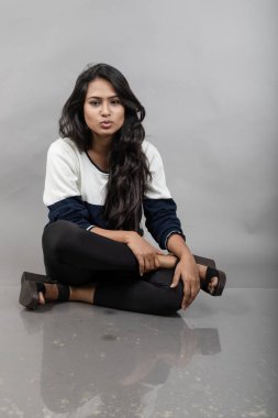 Gri arka planda günlük kışlık giysili Hintli genç bayan model. Siyah tayt giyen uzun siyah saçlı bir manken, mavi beyaz bir kazak..