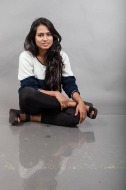 Gri arka planda günlük kışlık giysili Hintli genç bayan model. Siyah tayt giyen uzun siyah saçlı bir manken, mavi beyaz bir kazak..