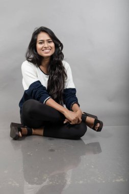 Gri arka planda günlük kışlık giysili Hintli genç bayan model. Siyah tayt giyen uzun siyah saçlı bir manken, mavi beyaz bir kazak..