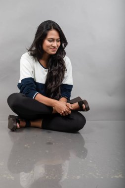 Gri arka planda günlük kışlık giysili Hintli genç bayan model. Siyah tayt giyen uzun siyah saçlı bir manken, mavi beyaz bir kazak..
