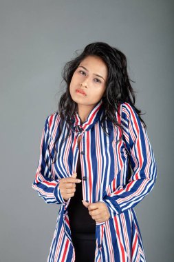 Gri stüdyo arka planında siyah, kırmızı, mavi, beyaz çizgili tunikli uzun siyah saçlı güzel bir kadın model.
