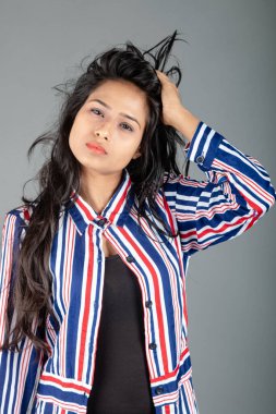 Gri stüdyo arka planında siyah, kırmızı, mavi, beyaz çizgili tunikli uzun siyah saçlı güzel bir kadın model.