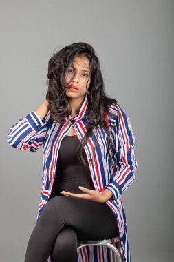 Gri stüdyo arka planında siyah, kırmızı, mavi, beyaz çizgili tunikli uzun siyah saçlı güzel bir kadın model.